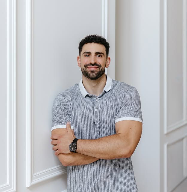 Stefan in a casual grey polo, standing by a panelled wall